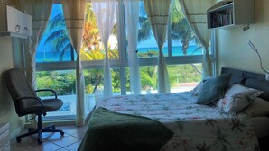 Un dormitorio con cama, una silla, una estantería y vistas al océano.