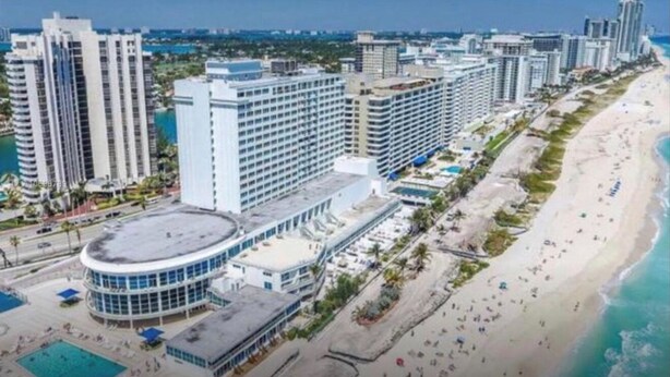 Un hotel costero con varios edificios altos, una playa y una zona de piscina.
