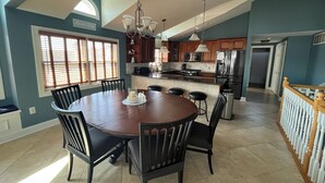 Une cuisine spacieuse dotée d’un grand îlot central, de meubles de rangement en bois foncé et d’un coin repas avec une table ronde et des chaises.
