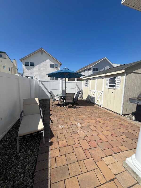A patio with a brick floor, outdoor furniture, and a blue umbrella.
