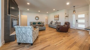 A spacious living room with hardwood flooring, a fireplace, and a large TV mounted on the wall. - Modern luxury home - on 1/2 acre near Kalahari (Hutto)