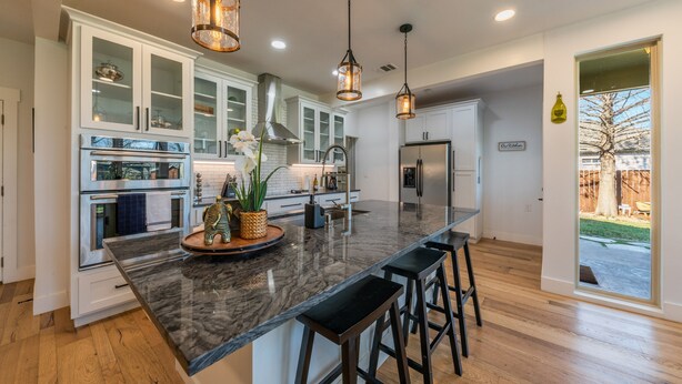 A modern kitchen with white cabinets, a marble island, and hanging pendant lights. - Modern luxury home - on 1/2 acre near Kalahari (Hutto)