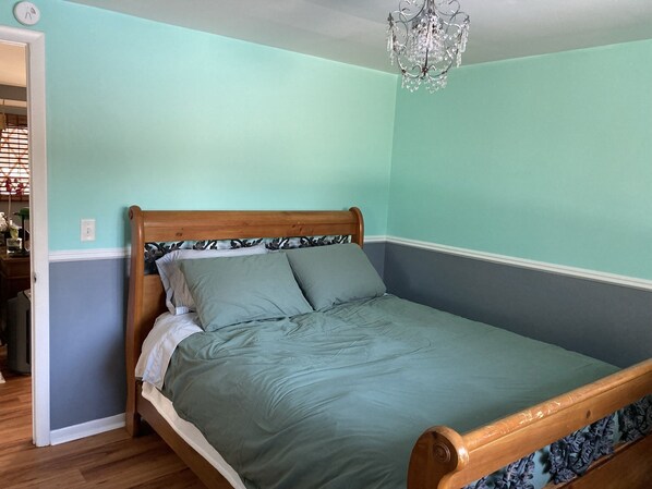 Een slaapkamer met een houten bedframe, turquoise wanden en een kroonluchter.