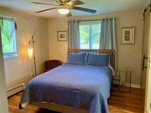 A bedroom with a bed, a ceiling fan, a standing lamp, and two windows with curtains.