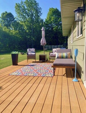 Una terraza de madera con mobiliario exterior, un tapete estampado y una planta en maceta.