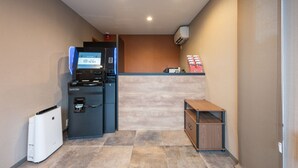Habitación de hotel compacta con kitchenette, una pequeña mesita de madera y un equipo de aire acondicionado integrado.