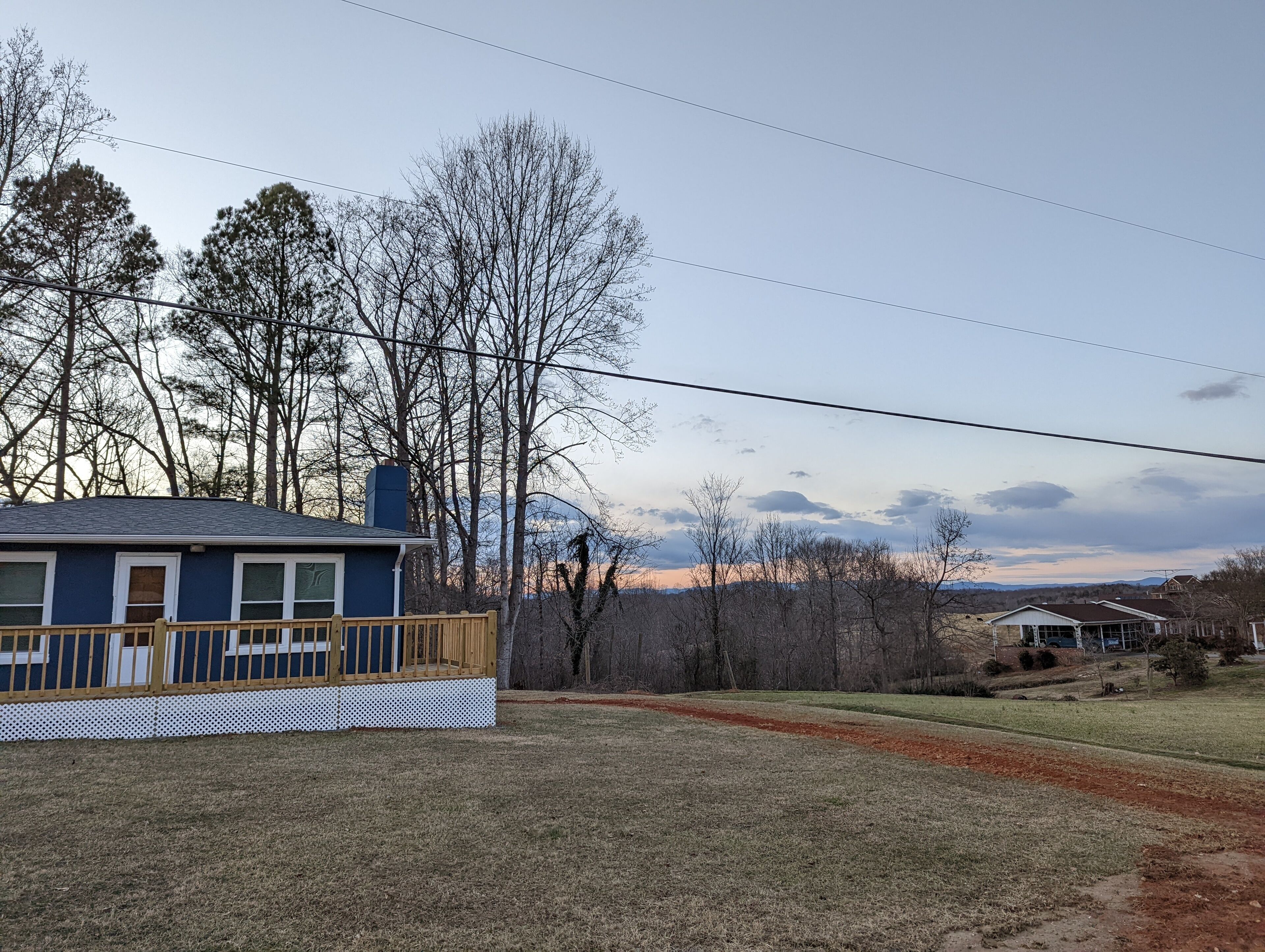 A house with a blue exterior, a wooden deck, and a view of trees and distant mountains.