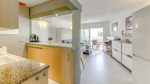 Ett modernt kök med bänkskivor i granit, träskåp och en köksö i mitten. I anslutning till köket finns en matplats med ett bord och stolar, som syns genom en öppen dörr.