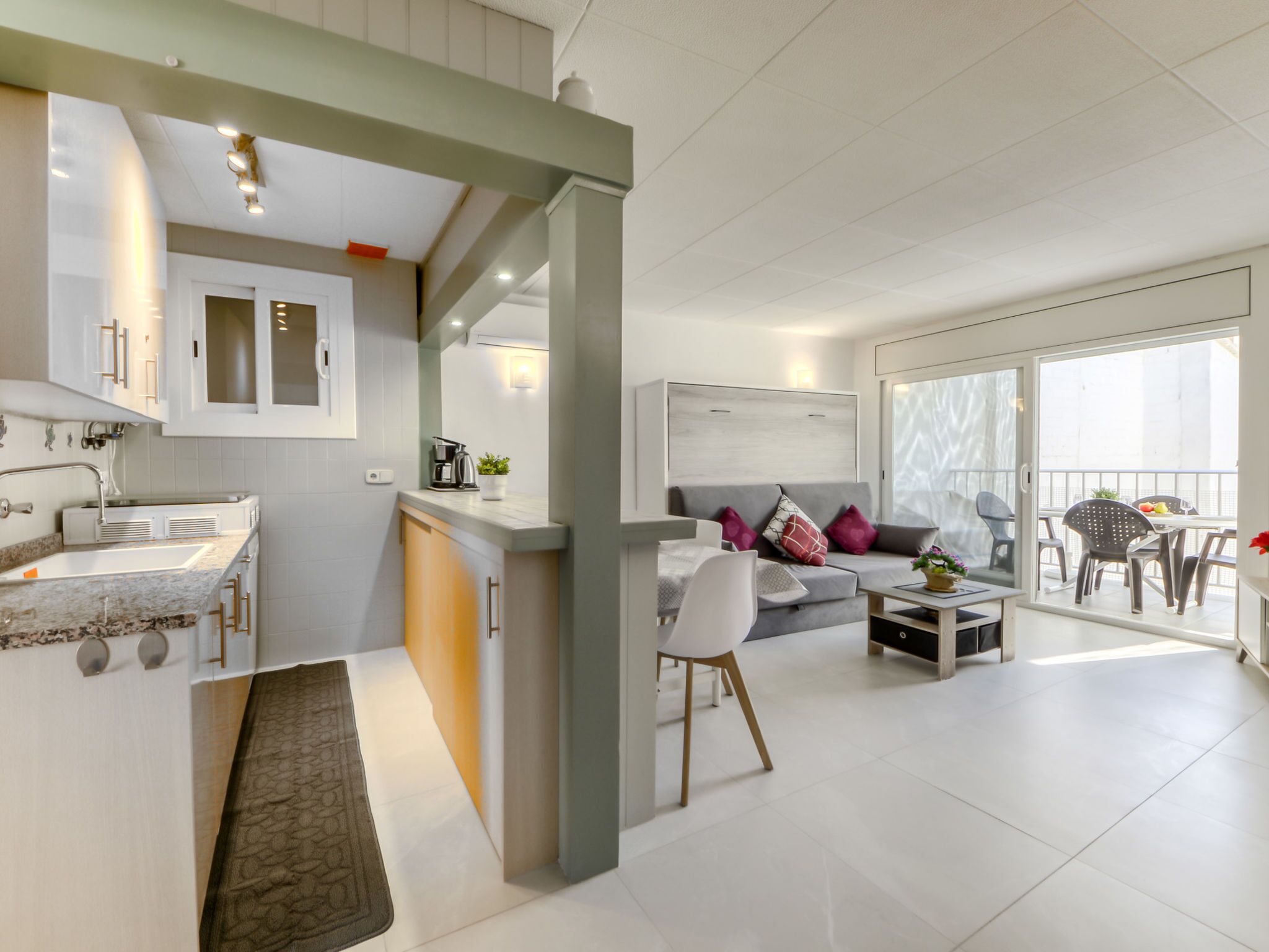 Un appartement moderne comprenant une cuisine, un coin repas et un salon. Il est doté d’une grande fenêtre, d’un canapé et d’une table basse.