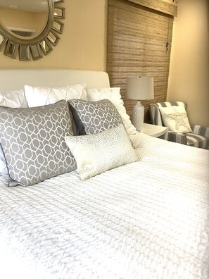 A neatly made bed with patterned pillows, a round mirror on the wall, and a lamp on a side table.