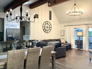 A spacious living room with a high ceiling, a chandelier, a clock, and a sign reading "Welcome to The Lake House".