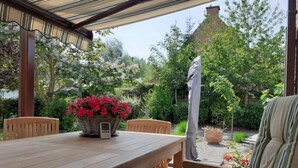 Un patio exterior con mesa y sillas de madera, una cesta de flores rojas y una pérgola.