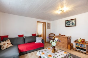 Una sala de estar con un sofá, un aparador de madera, una mesita con un jarrón y una estantería.