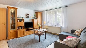 Un salon comprenant un téléviseur, des meubles en bois, un canapé et une table sur laquelle est posé un vase.