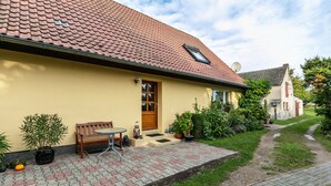 Une maison avec un toit en tuiles, un banc en bois et des plantes en pot.