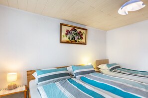 Habitación de hotel con dos camas, una mesita de noche con lámpara, un cuadro floral enmarcado en la pared y una lámpara de techo.