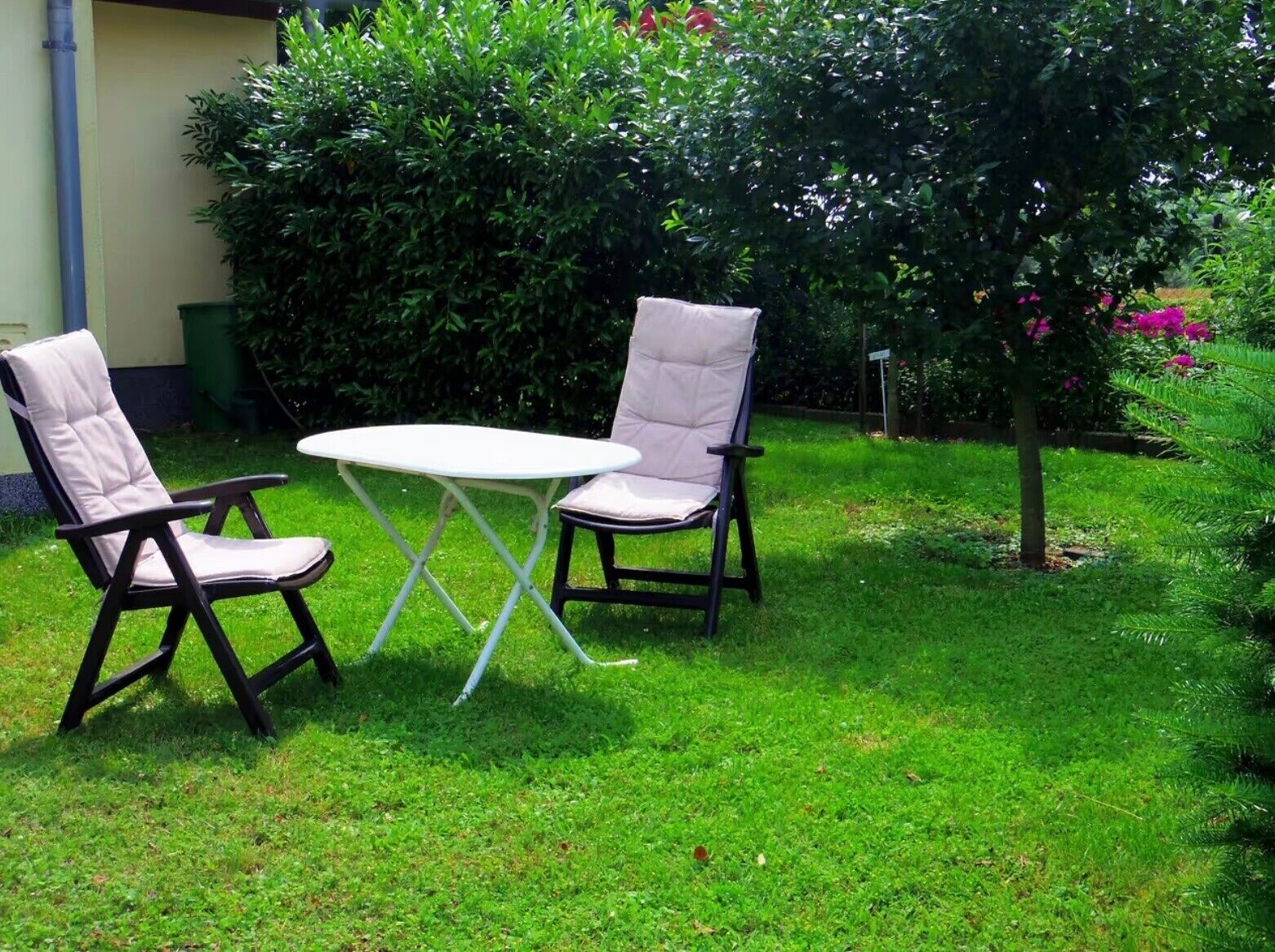 Ein Sitzbereich im Freien mit zwei Stühlen und einem Tisch, umgeben von Gras und Pflanzen.
