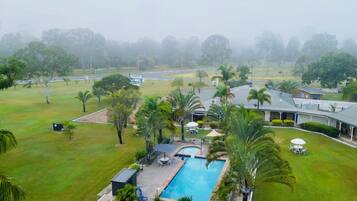 A hotel with a swimming pool, outdoor seating, and a view of a road and trees.