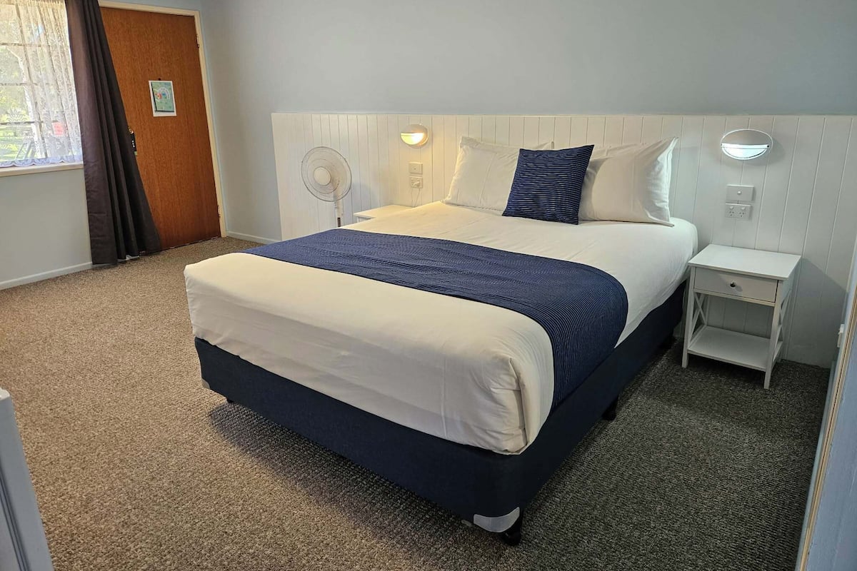Een hotelkamer met een bed, nachtkastjes, een ventilator aan de muur en een raam met gordijnen.