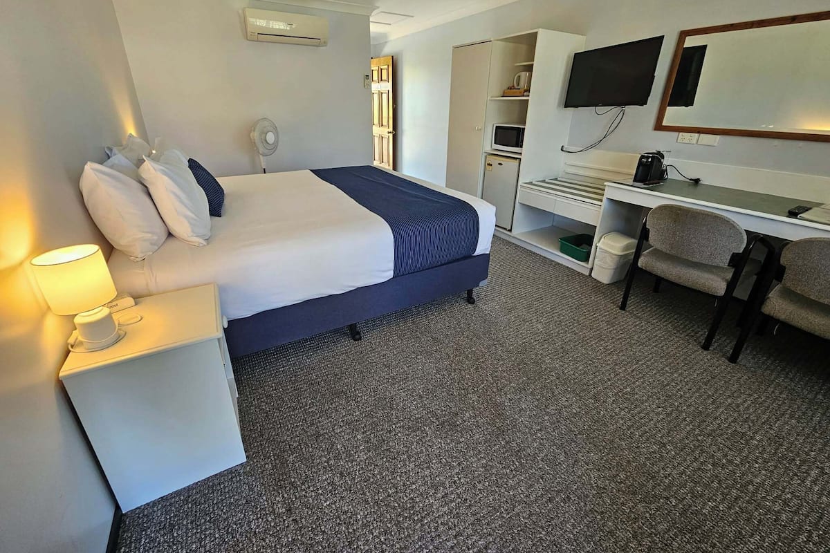 Een hotelkamer met een bed, bedlampje, bureau, stoel, televisie en een klein kitchenette.