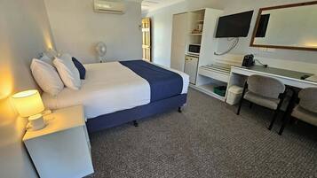 Ein Hotelzimmer mit Bett, Nachttischlampe, Schreibtisch, Stuhl, Fernseher und einer kleinen Küchenzeile.