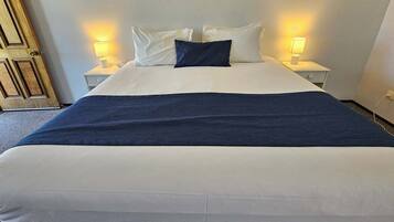 A hotel room with a large bed, two bedside tables with lamps, a wooden door, and a carpeted floor.