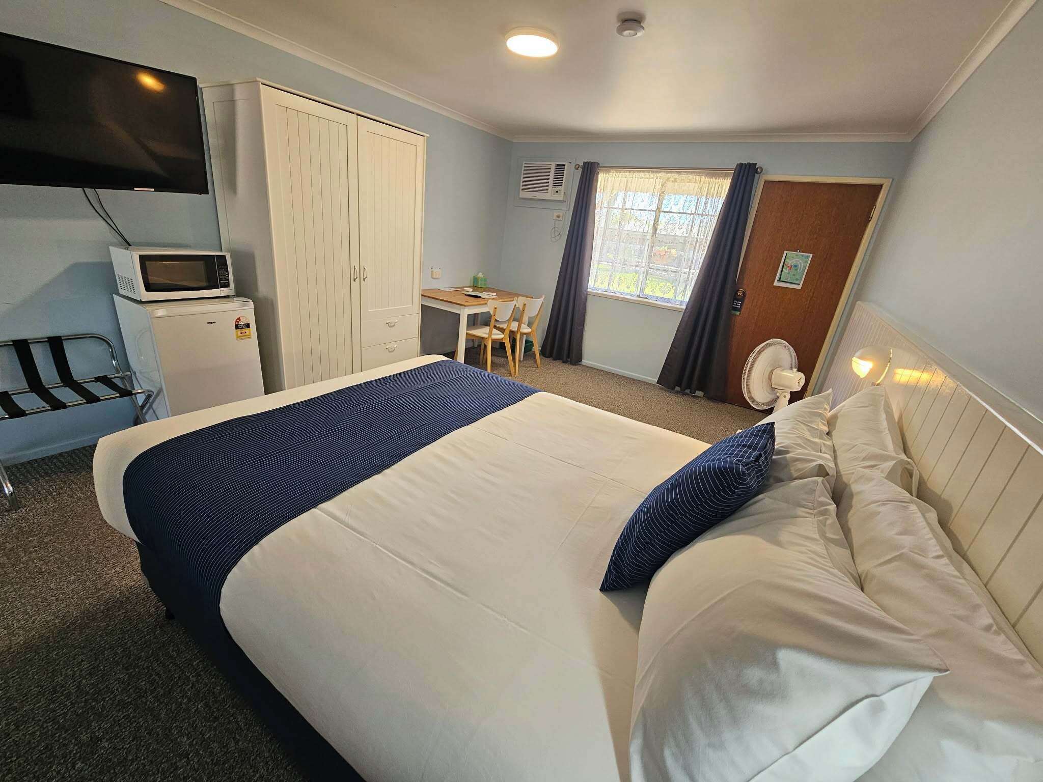 A hotel room with a bed, a desk, a television, a wardrobe, and a window with curtains.