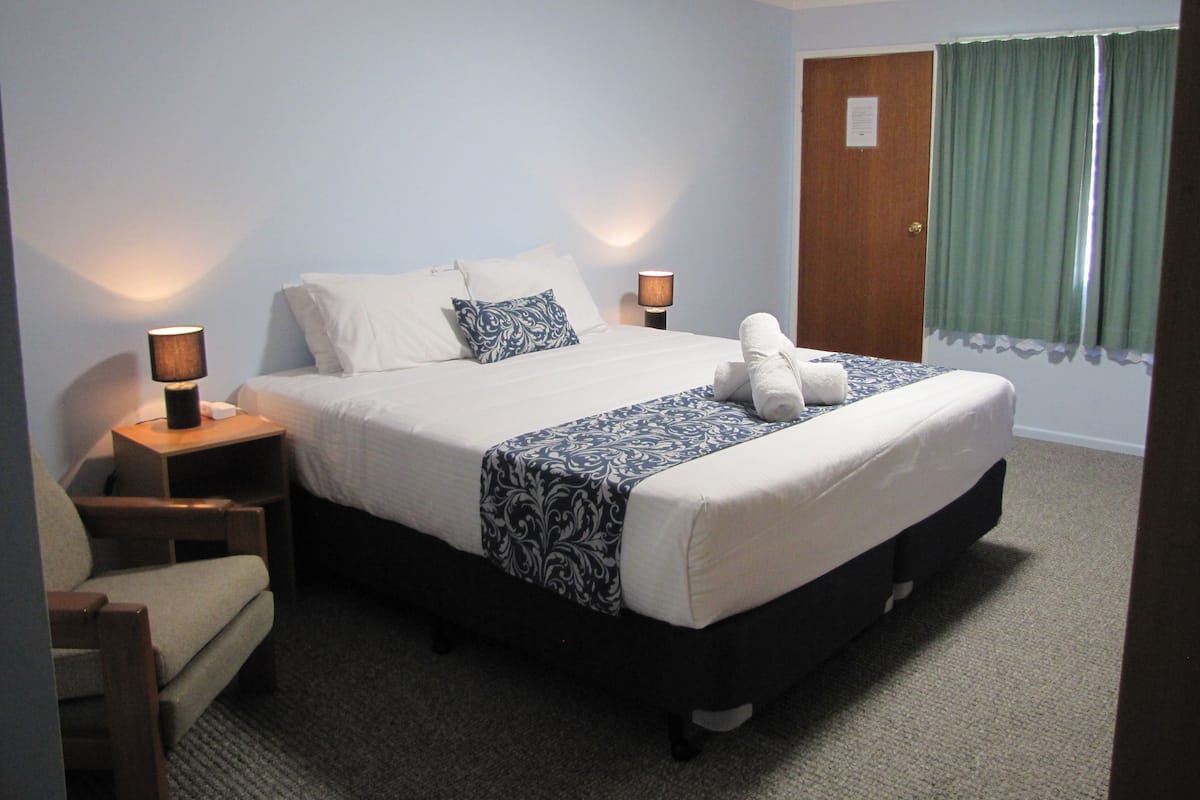 Een hotelkamer met een bed, twee nachtkastjes, een stoel, een raam met gordijnen en een deur.
