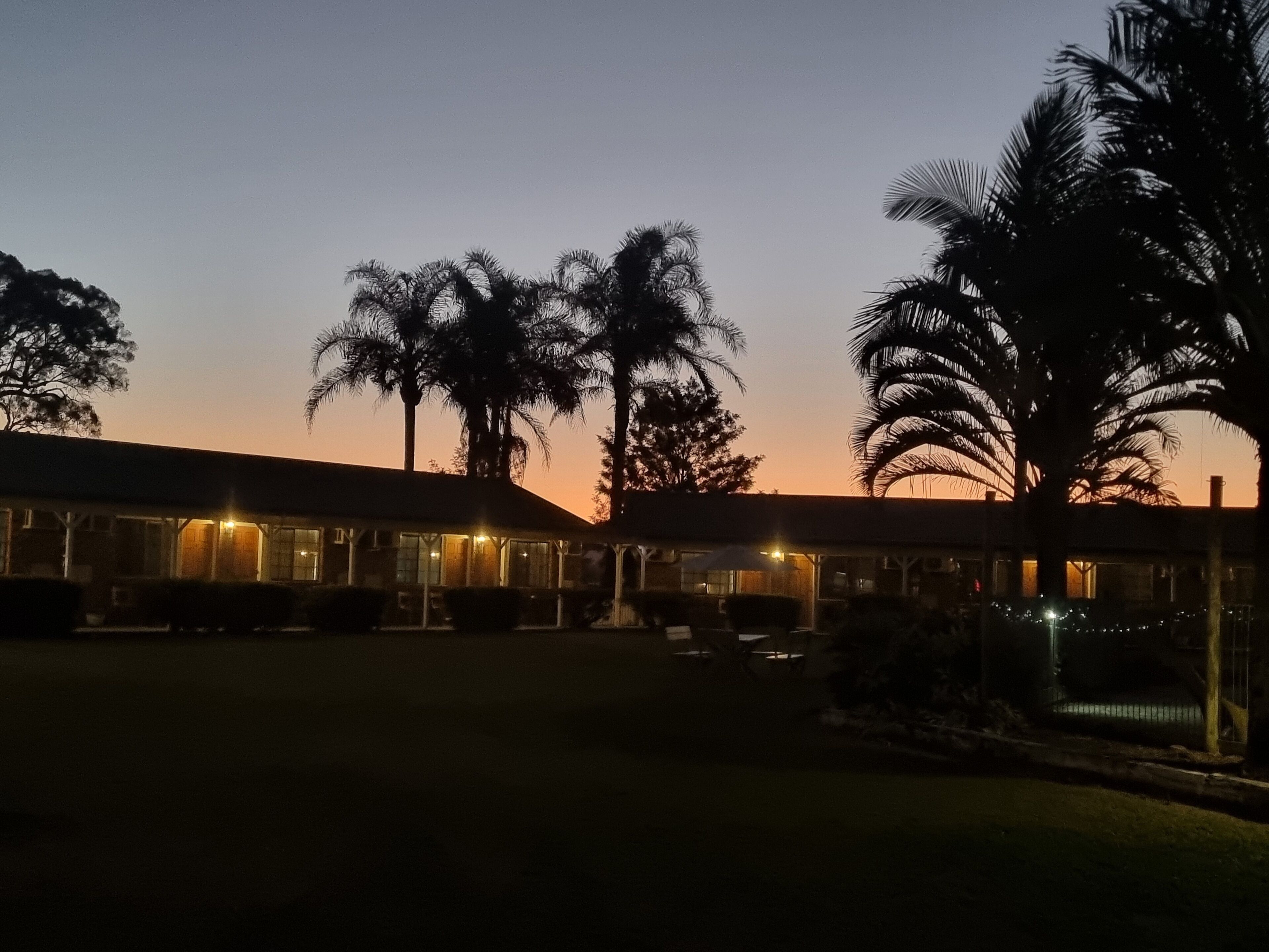Un edificio con una zona esterna coperta, palme e un tramonto sullo sfondo.