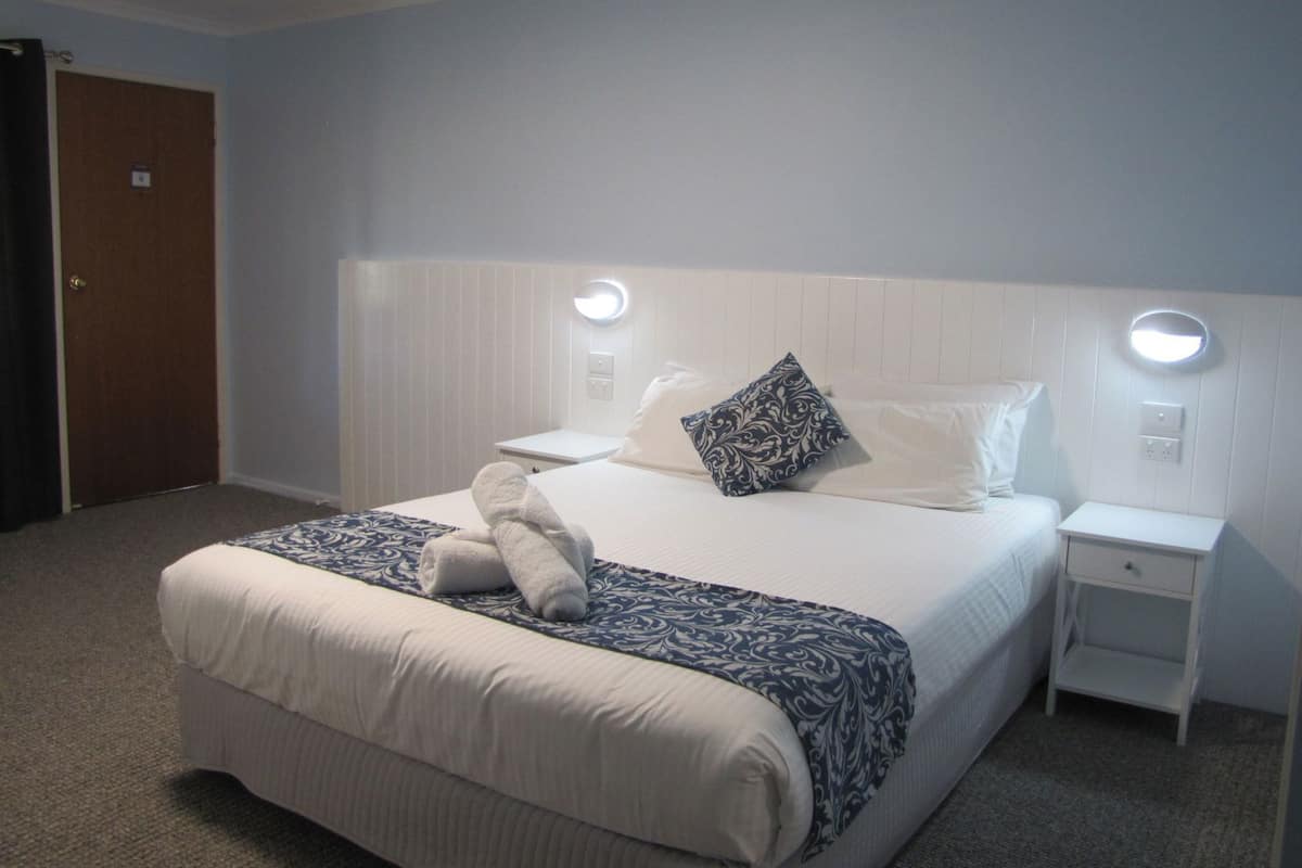 Een hotelkamer met een bed, nachtkastjes, een nachtlampje, een deur en een wandlamp.