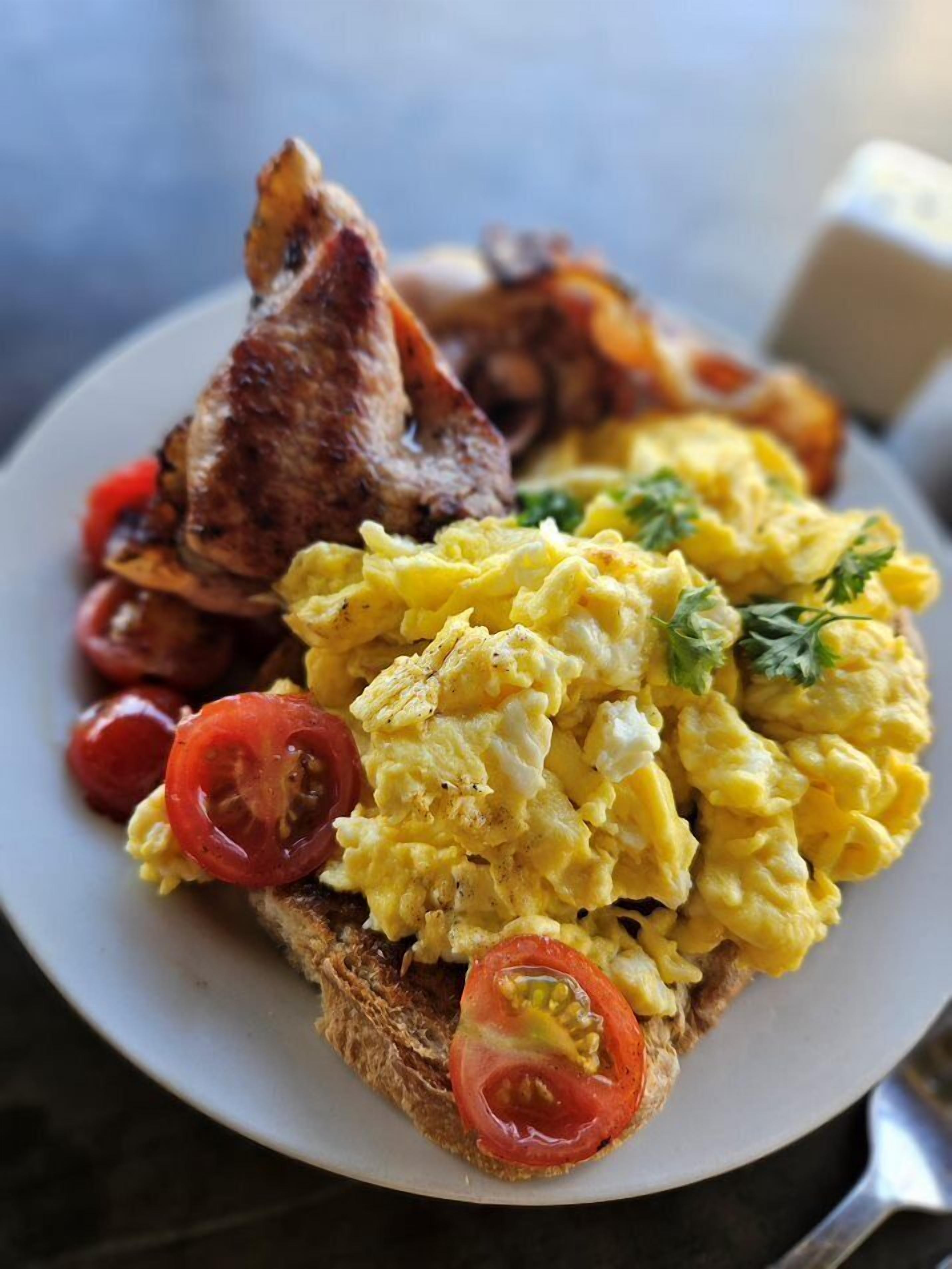 A plate with scrambled eggs, grilled meat, and toast with tomato slices.