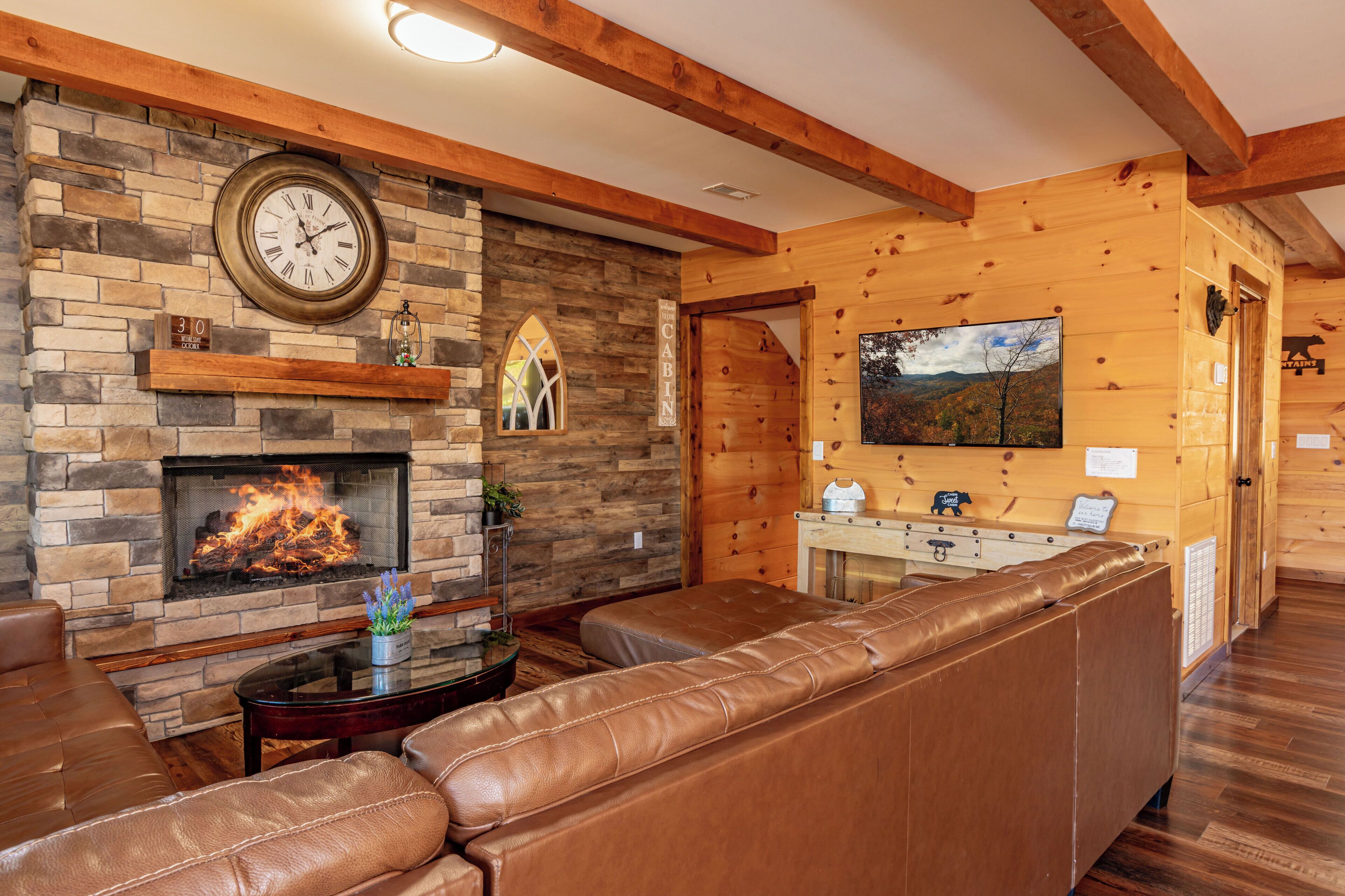 Ein gemütliches Blockhäuschen mit Kamin aus Stein, Ledersofa, Holzwänden und einer Wanduhr.