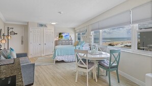 Ein Zimmer mit einem Bett, einem Esstisch und Blick auf den Strand.