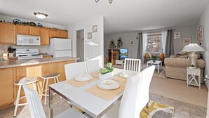 Una cocina moderna con armarios de madera, una encimera blanca y un comedor con mesa y sillas blancas.