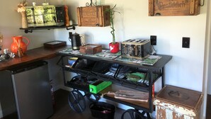 Uma cozinha com um carrinho de madeira, cafeteira, torradeira e diversos utensílios de cozinha nas prateleiras.