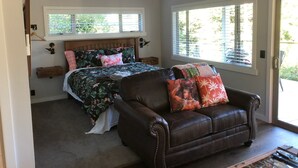 Quarto com uma cama, um sofá de couro e uma janela com persianas.