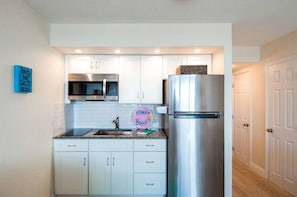 A compact kitchen with white cabinets, a stainless steel refrigerator, a microwave, and a sink. - Aloha Hibiscus Room,Sunset Views w/ Balcony #442 (Daytona Beach Shores)