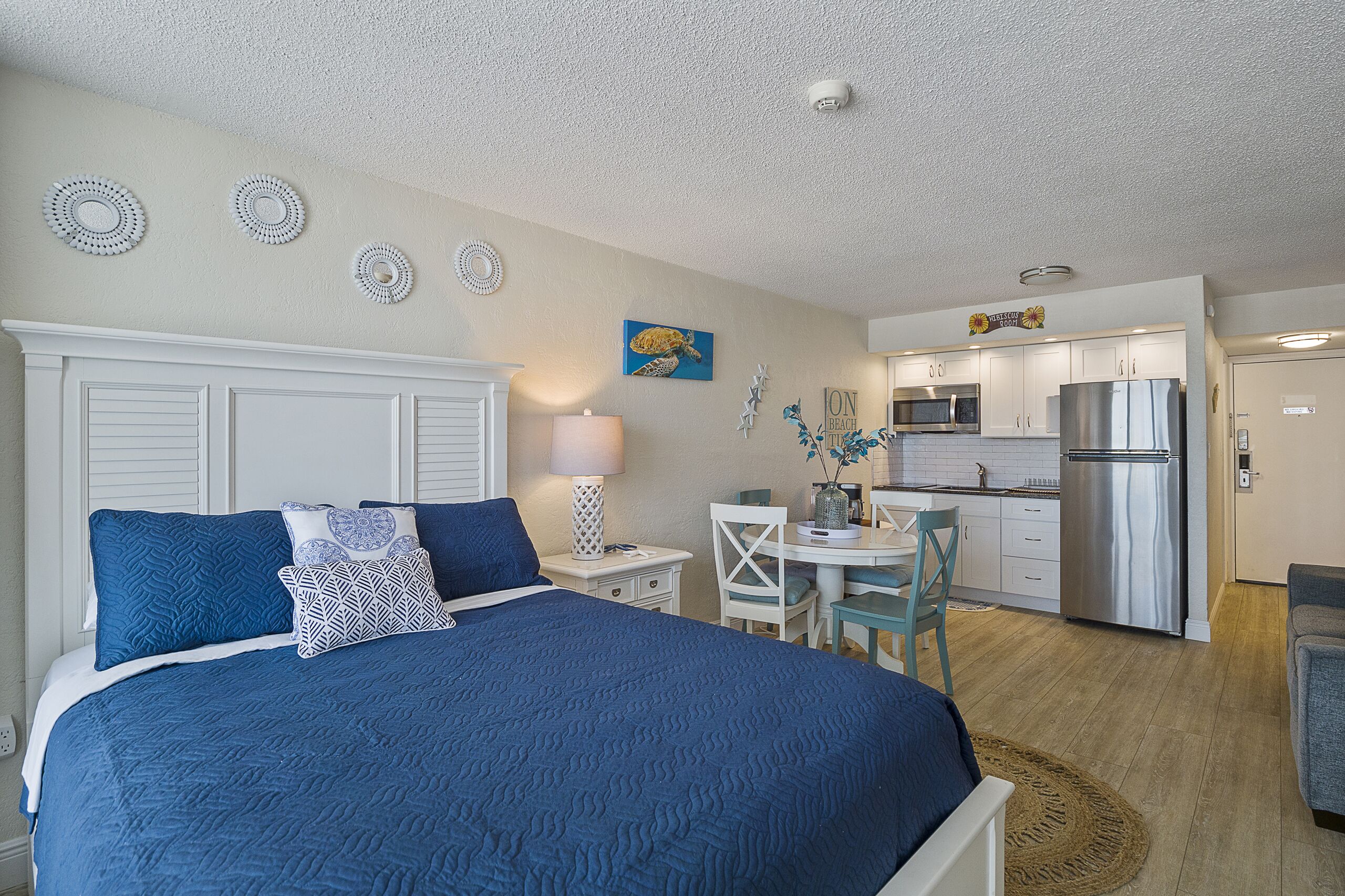 A bedroom with a large bed, a desk, and a kitchenette.
