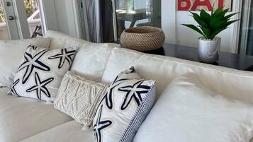 A white sofa with starfish pillows, a woven basket, and a potted plant.