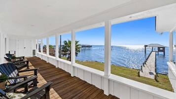 A covered outdoor area with wooden flooring and white railings, overlooking a body of water with a pier and a gazebo.