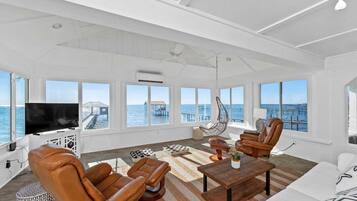 A spacious living room with a large TV, leather chairs, a hanging chair, and a view of the ocean through large windows.