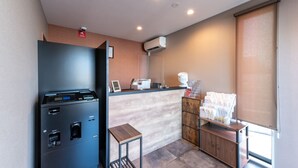 A compact kitchen with a built-in espresso machine, a small table, and a wooden cabinet with storage. - HOTEL R9 The Yard Hitachinaka (Hitachinaka)