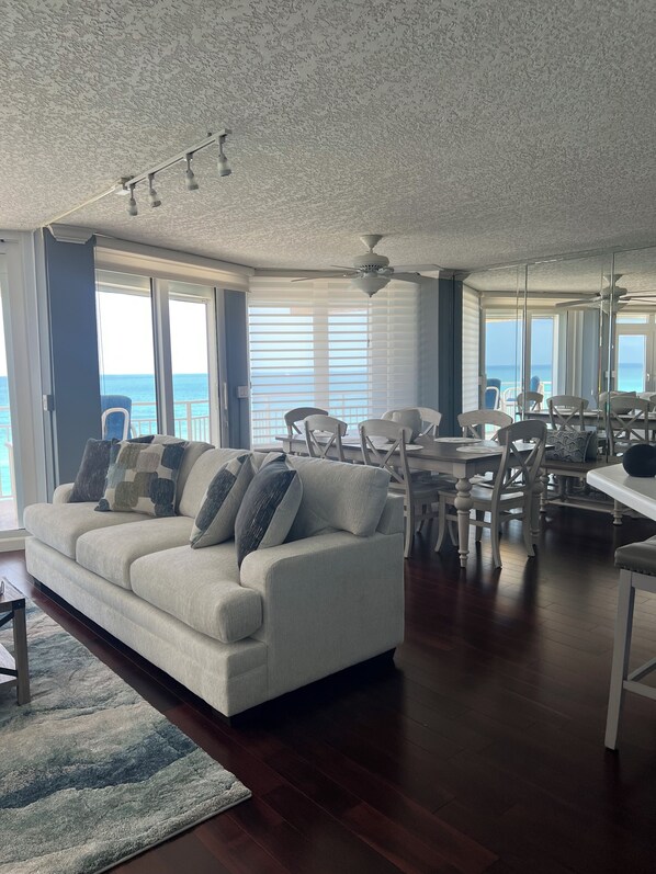 A spacious living room with a white sofa, dining area, and large windows offering a view of the ocean.