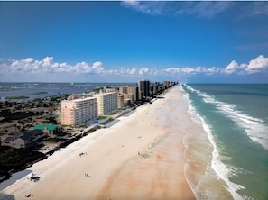 Un paysage urbain côtier avec une longue plage, de grands hôtels et un ciel dégagé.
