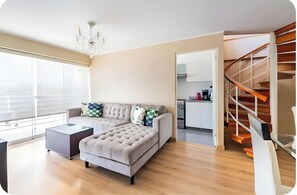 A modern living room with a sofa, coffee table, and a staircase leading to an upper level. - Barranco Duplex Penthouse (Barranco)