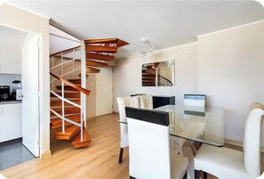 A modern interior with a spiral staircase, a dining area with a glass table, and a kitchen in the background.