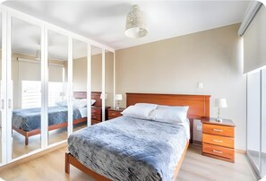 A bedroom with a large bed, a wardrobe, a bedside table, and a lamp.