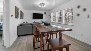 Una sala moderna con una mesa de comedor de madera, un sofá gris y un televisor de pantalla plana montado en la pared.