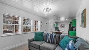 Una sala de estar moderna con un sofá seccional gris, almohadas a rayas verdes y azules, y un comedor con una mesa y sillas de madera.