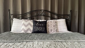 Una cama con un colcha estampada y cuatro almohadas con distintos diseños, una de ellas con el texto "live SIMPLY".